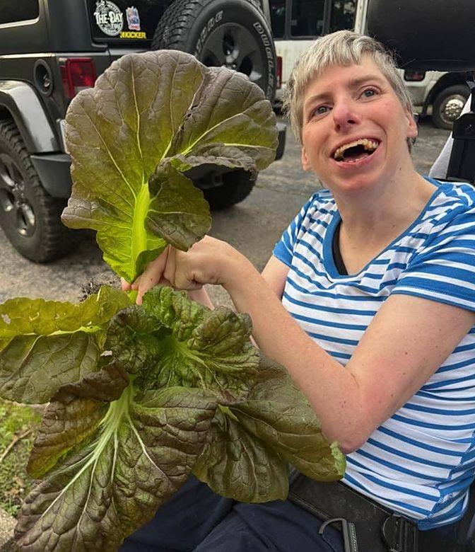A member laughing while holding huge lettuce leaves she grew