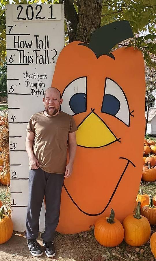 A member laughing next to a giant pumpkin cutout at the pumpkin patch