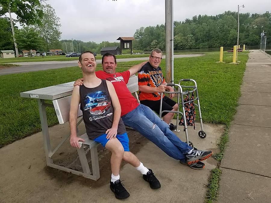 Three friends laughing together on a park bench by the river