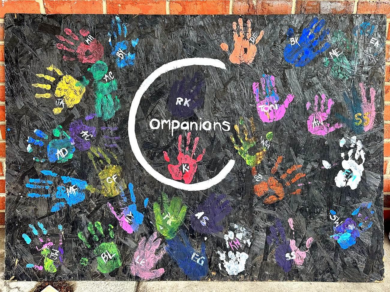The Companions handprint wall, covered in colorful handprints with members' initials