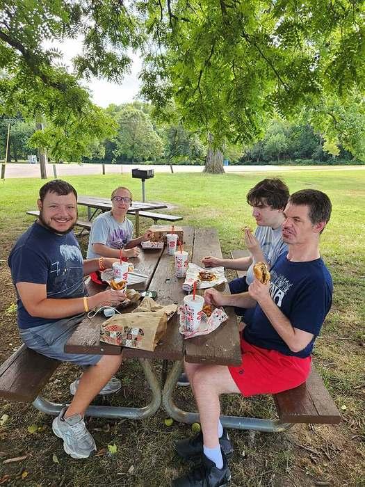 Four members enjoying a meal together at a shaded picnic table